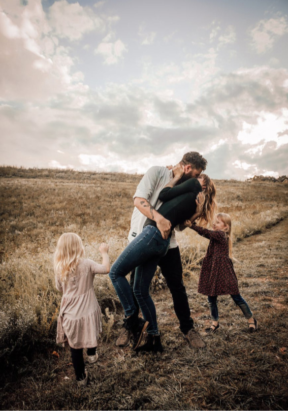 a family in a farm field while the husband kisses his wife.